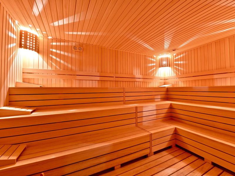 Intérieur d'un sauna en bois clair avec bancs en plusieurs niveaux et éclairage chaleureux.