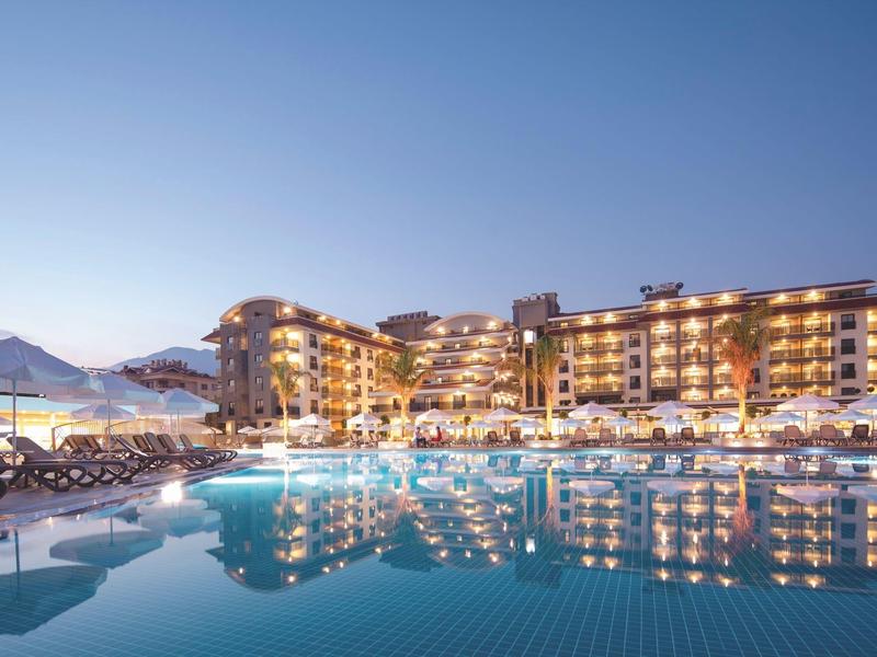 Hôtel moderne avec piscine éclairée et chaises longues sous un ciel clair du soir.