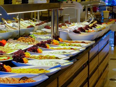 Buffet mit verschiedenen Salaten und Beilagen in großen weißen Schalen auf Holztresen präsentiert.