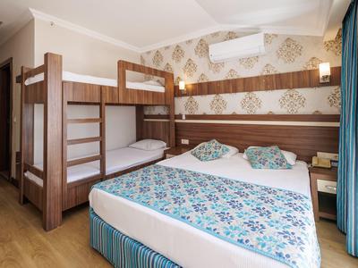 Hell eingerichtetes Schlafzimmer mit Etagenbett, Doppelbett, blauen Vorhängen und gemusterter Bettwäsche.