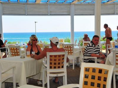 Offenes Restaurant mit weißen Tischdecken und Holzstühlen mit Meerblick und Gästen.