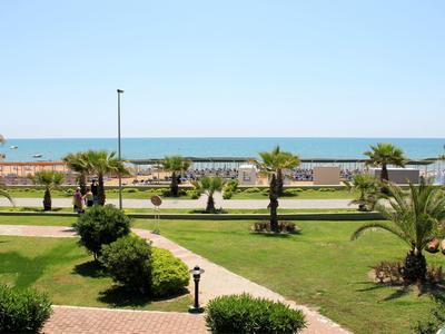 Strandpromenade mit Palmen, Grünflächen und blauem Meer im Hintergrund bei klarem Himmel.
