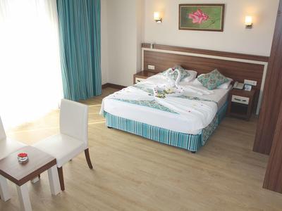 Helles Hotelzimmer mit großem Bett, zwei weißen Stühlen, kleinem Tisch und Bodenvorhängen.