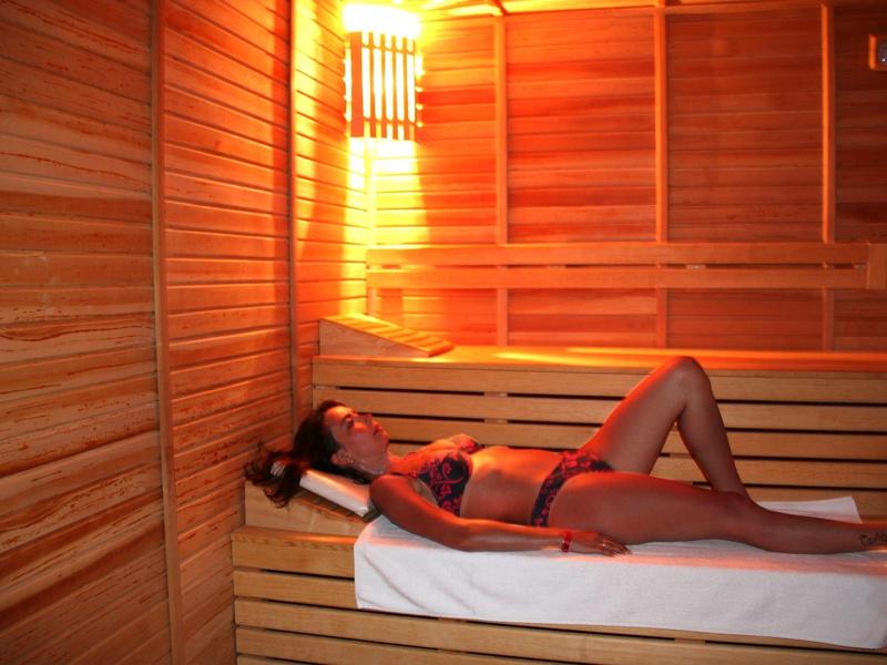 Woman relaxing in bikini on wooden bench in warmly lit sauna.