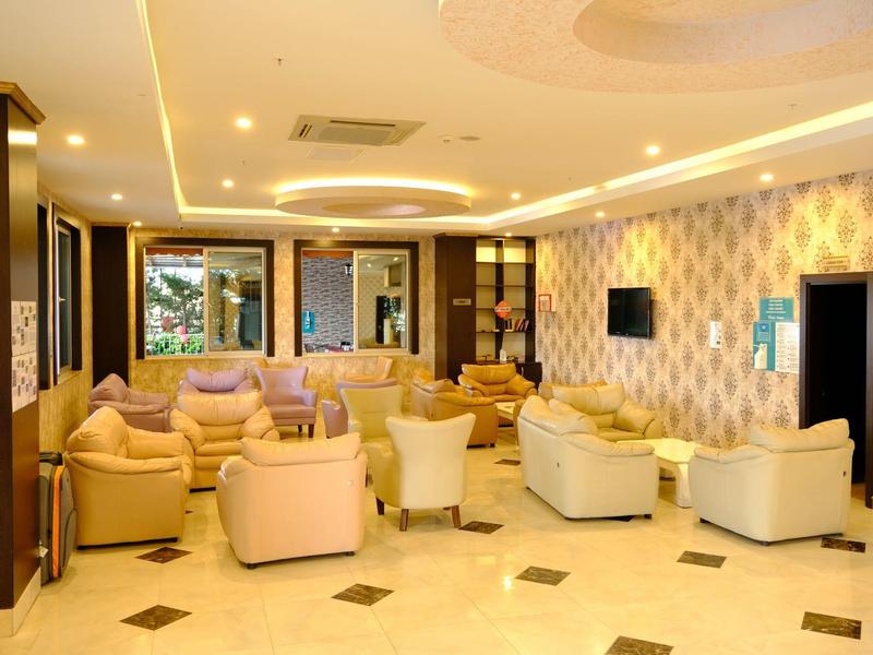 Elegant hotel lounge area with beige armchairs, modern lighting, and wall-mounted TV.