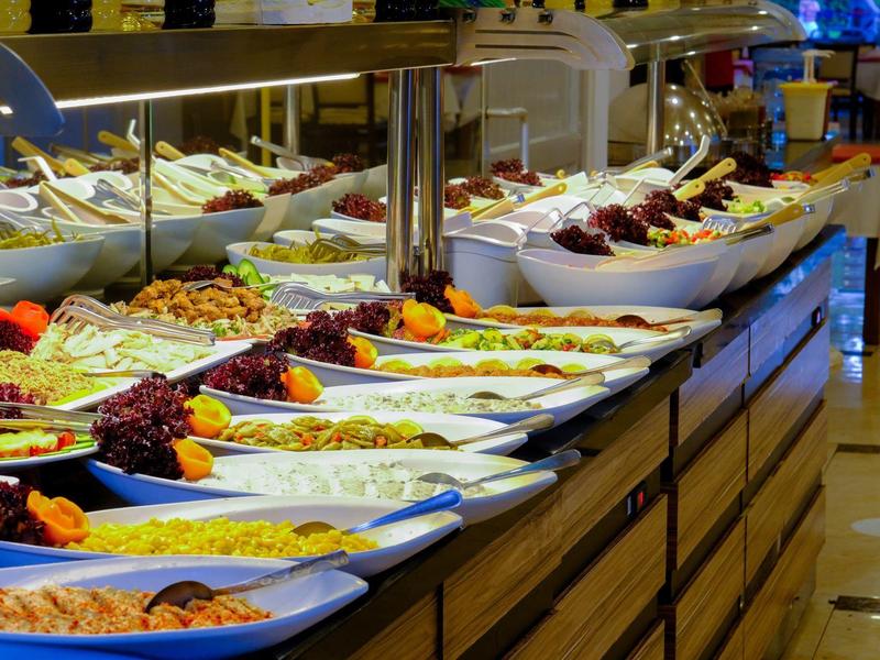 Buffet with a variety of colorful dishes in white bowls on a long wooden table.