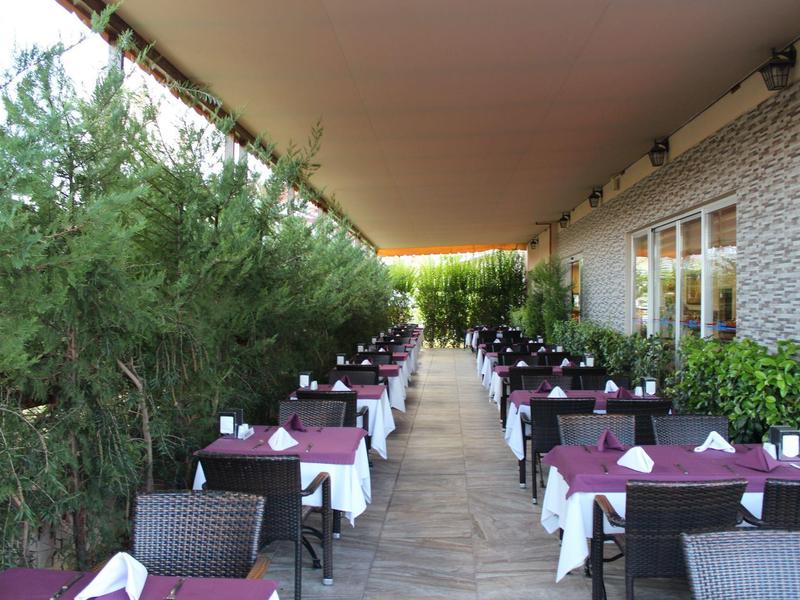 Outdoor restaurant area with set tables and chairs along a green wall.