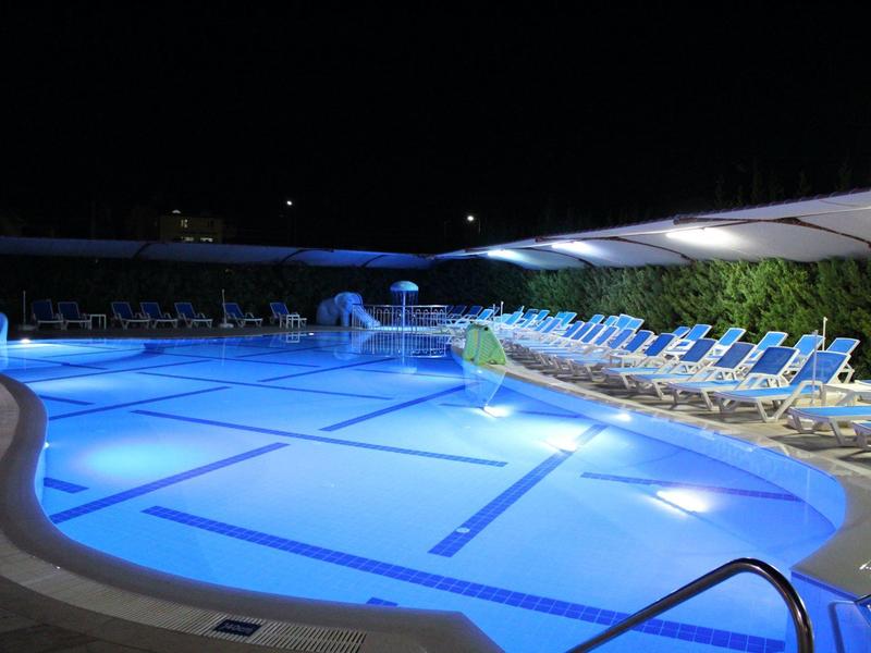 Illuminated hotel pool with lounge chairs at night under clear sky.