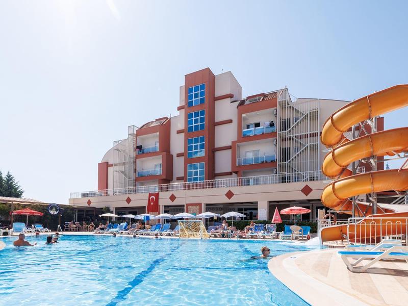 Large outdoor pool with water slide and sun umbrellas in front of multi-story hotel building