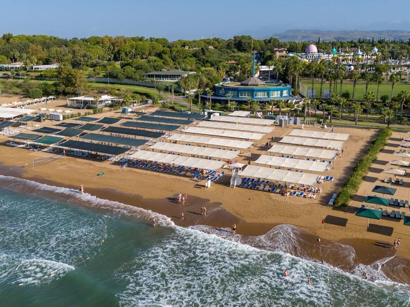 Beach with umbrellas and loungers in front of a hotel with green gardens