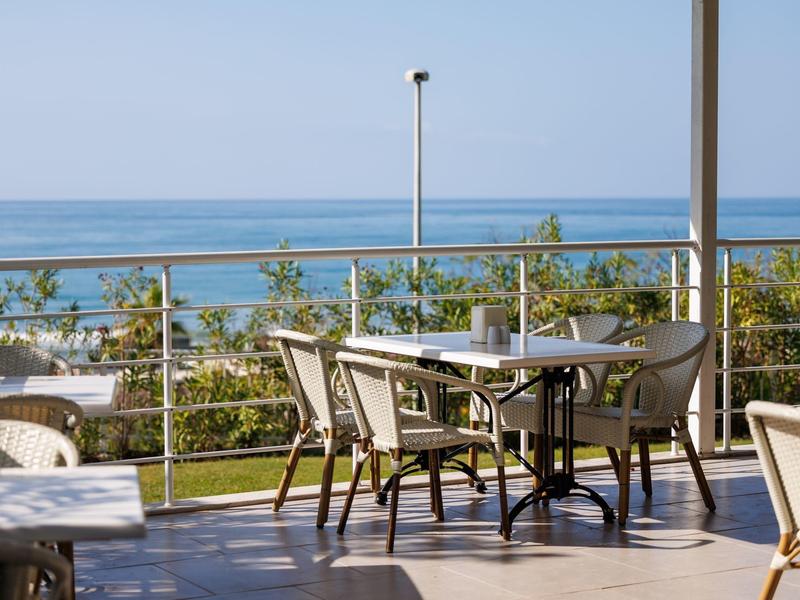 Terrace with tables and chairs overlooking the sea on a clear day.