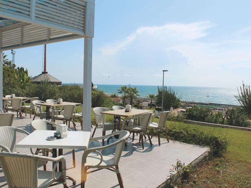 Outdoor terrace with tables and chairs, overlooking the sea and garden