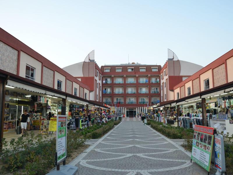 Spacious shopping area with shops and a walkable central path, surrounded by multi-story buildings.