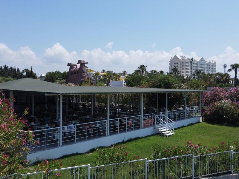 Modern pavilion with glass facade in green, blooming garden under blue sky