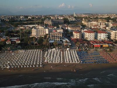 Blick auf einen Strand mit Reihen von Liegestühlen und dahinter städtische Gebäude bei Sonnenuntergang.