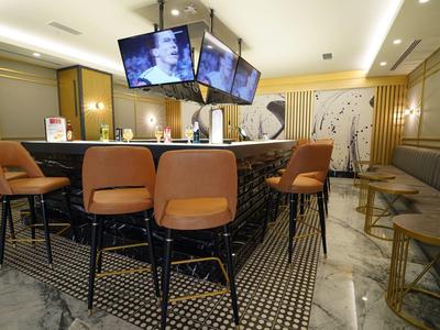 Moderner Hotelbarbereich mit braunen Ledersesseln und mehreren Bildschirmen über der Theke.