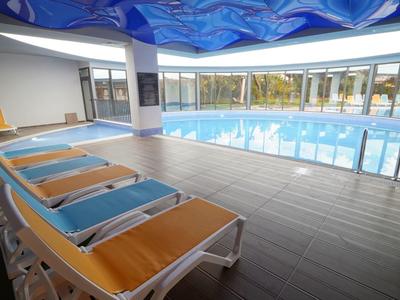Hallenbad mit Liegestühlen am Rand und großer Fensterfront mit Außenblick.