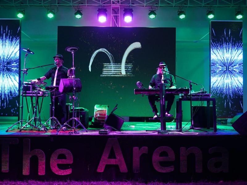 Band spielt live auf einer Bühne mit Gitarren und Tastatur, beleuchtet von bunten Lichtern.