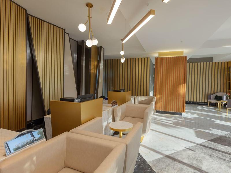 Moderne Hotellobby mit beigen Sesseln, goldenen vertikalen Wandpaneelen und stilvollen Leuchten.