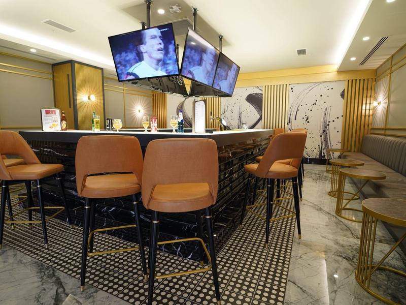 Moderner Hotelbarbereich mit braunen Ledersesseln und mehreren Bildschirmen über der Theke.