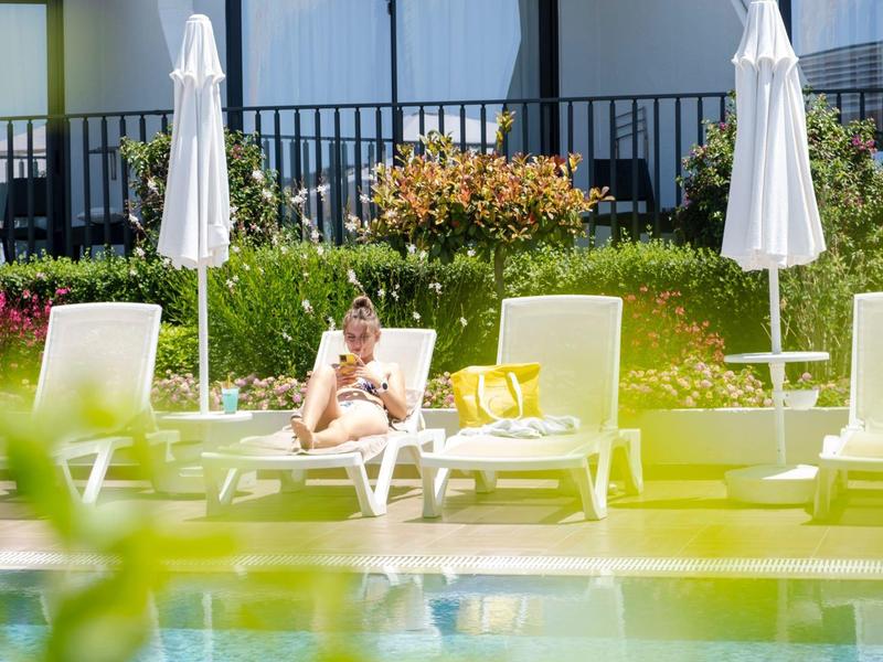Frau entspannt auf Liegestuhl neben Pool mit Sonnenschirmen und Garten im Hotel