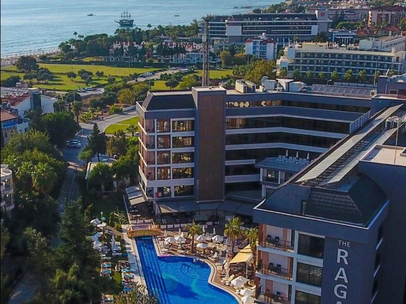 Blick auf ein Hotel mit Pool und Meer im Hintergrund an einem sonnigen Tag.