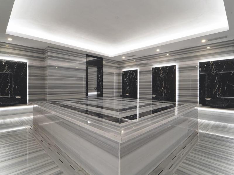 Modernes Hammam mit grauem und schwarzem Marmor, sanfter Beleuchtung und Wasserbecken.