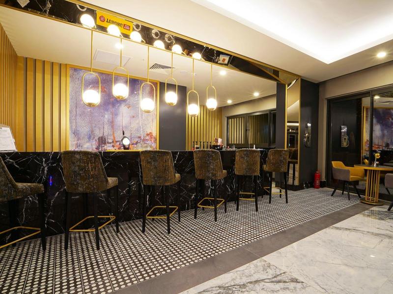 Elegante Hotelbar mit goldenen Akzenten und modernen Hockern auf gemustertem Boden.