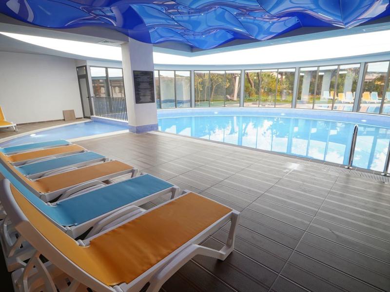 Hallenbad mit Liegestühlen am Rand und großer Fensterfront mit Außenblick.