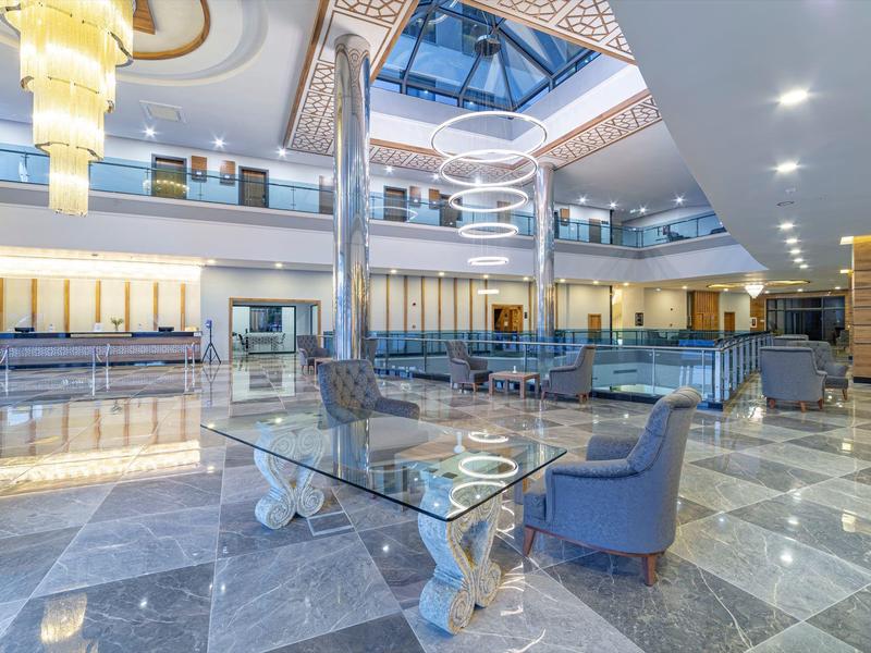 Große Lobby mit glänzendem Marmorboden, Glas-Tisch, blauen Sesseln und hellem Deckenlicht.