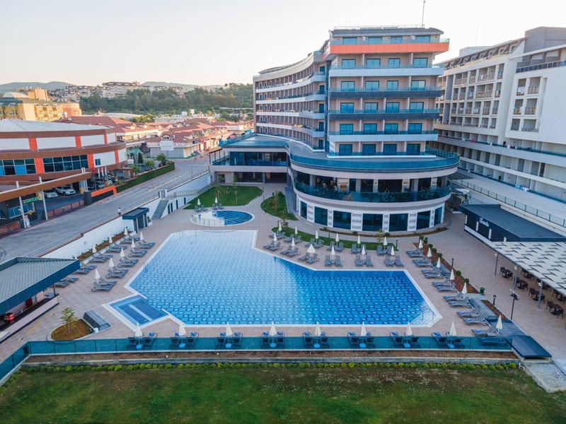 Großes Hotel mit mehrstöckigem Bau, großem Pool, Liegestühlen und umliegender Stadtlandschaft.