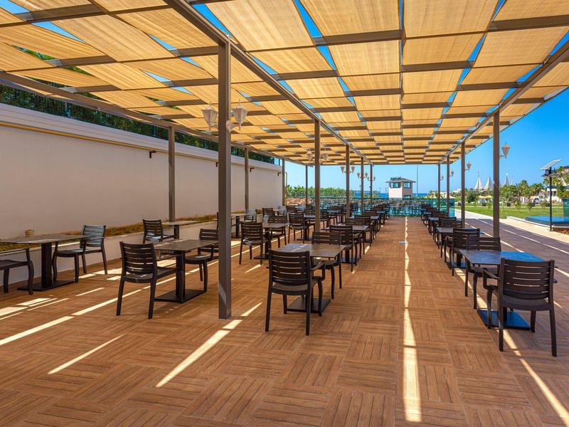 Überdachter Außenbereich mit Reihen von schwarzen Stühlen und Tischen neben einem Pool bei Sonnenschein.