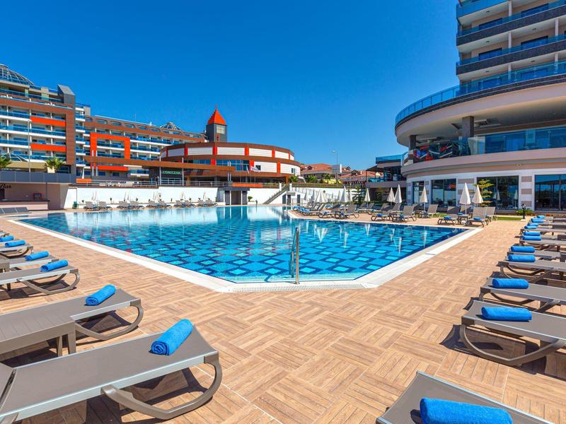 Großer Außenpool mit blauen Liegestühlen und modernen Hotelgebäuden unter klarem Himmel.