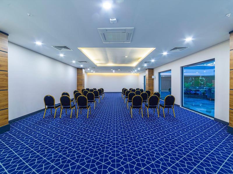 Moderner Tagungsraum mit blaugeflittertem Teppich, Stühlen in Reihen und großem Fenster.