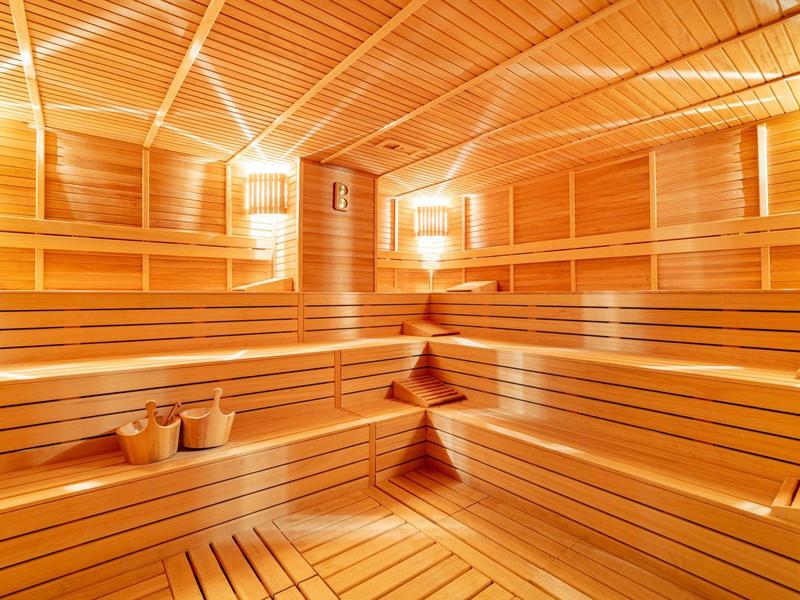 Helle Sauna mit Holzverkleidung, mehrstufigen Bänken und zwei Holzeimern auf Boden.