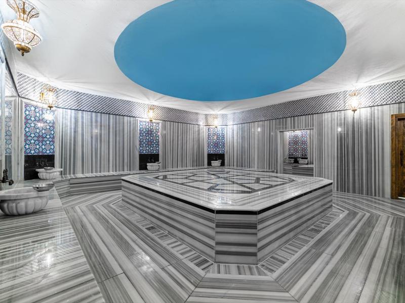 Großer Hamam mit grauen Marmorfliesen, blauem Deckengewölbe und zentralem beheiztem Marmorblock.