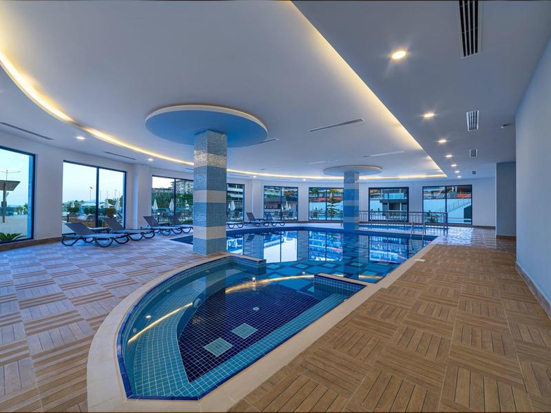 Moderner Innenpool mit blauem Wasser, großen Fenstern und entspannenden Liegestühlen.