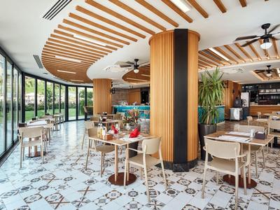 Bright restaurant with large windows, wooden ceiling, and modern furniture by the water.