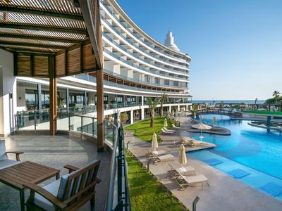 Modern hotel structure with a large pool area and sun umbrellas under clear sky.