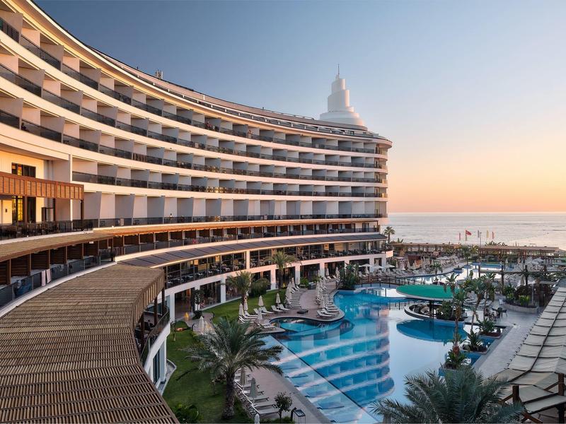 Modern hotel with curved facade and lit pool at sunset.