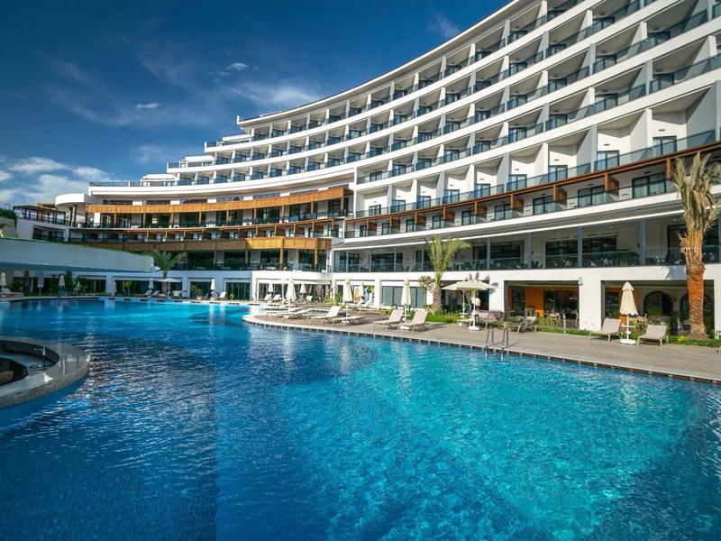 Modern hotel with curved design and large pool under blue sky.