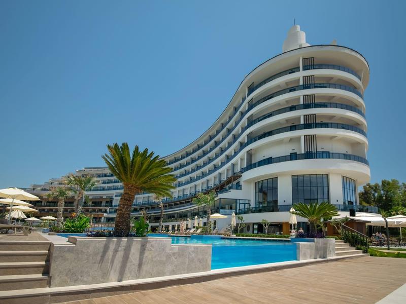 Modern hotel with curved facade and outdoor pool under clear blue sky.