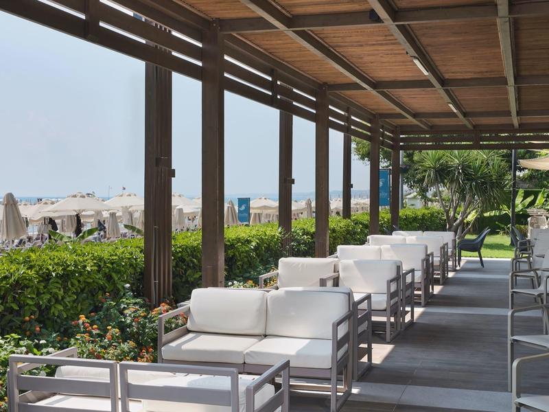Covered terrace with white seating and view of the sea and beach.
