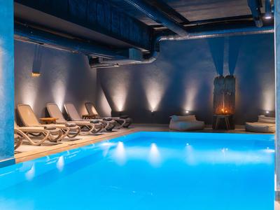 Vnitřní bazén s modrým osvětlením a lehátky v moderní hotelové spa oblasti.