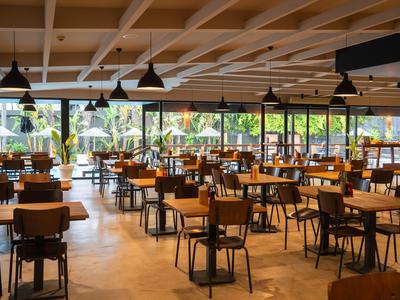 Prostorná restaurace s dřevěnými stoly a židlemi, velkými okny a výhledem na zelené venkovní prostory.