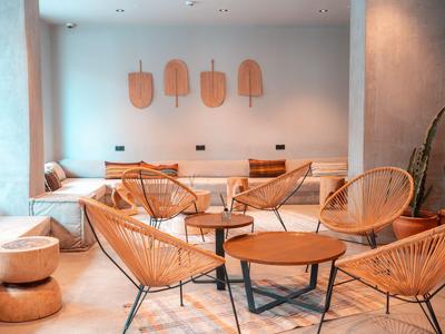 Moderní hotelová lounge s ratanovými židlemi, kulatými stoly a pohodlným posezením u stěny.