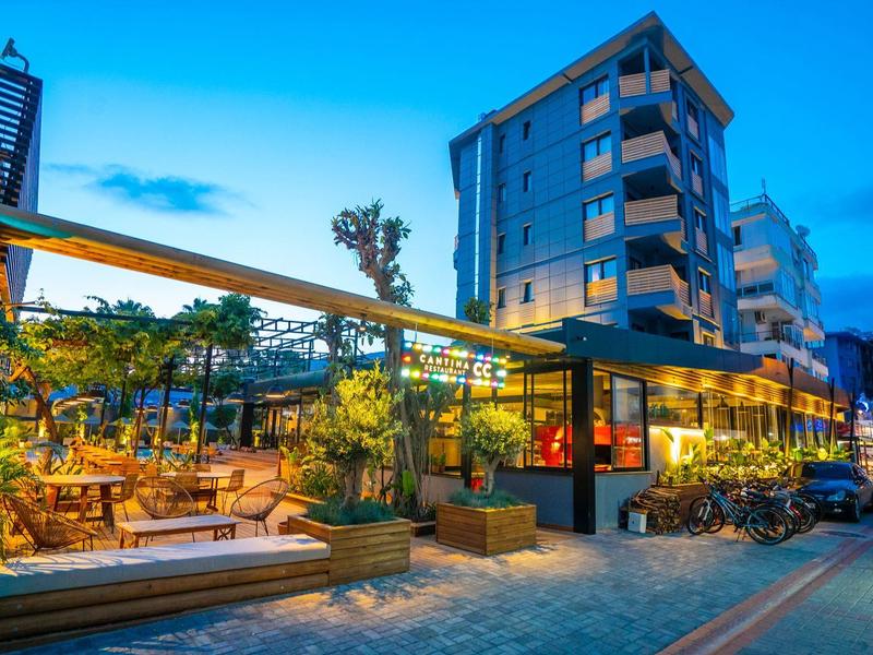 Modern hotelcomplex met verlichte buitenterras en zitplaatsen bij schemering.