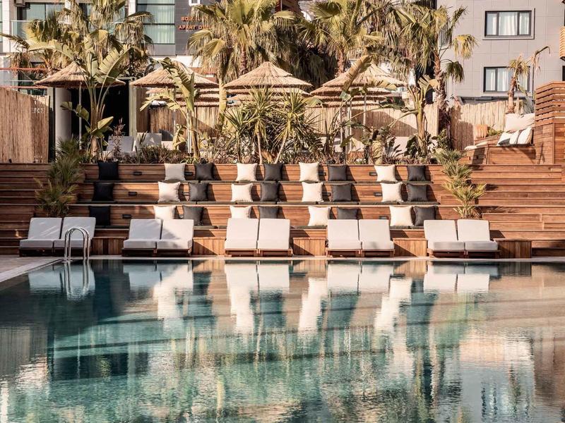 Hotelzwembad met witte ligstoelen en palmbomen in een zonnige, moderne omgeving.