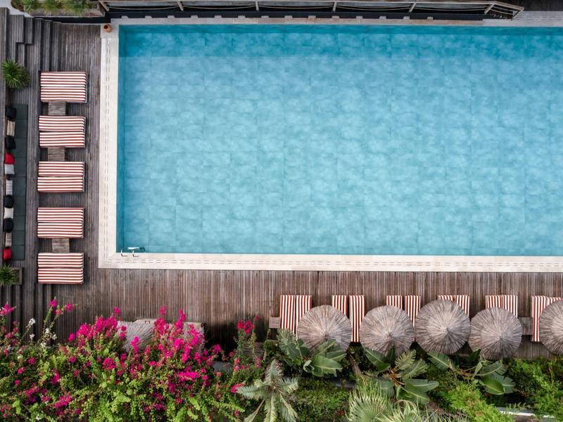 Luchtfoto van een rechthoekig zwembad met ligstoelen en weelderige beplanting eromheen.