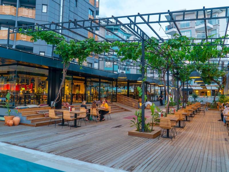 Moderne hotelterras met houten vloer, bomen, zitgedeeltes en uitzicht op een zwembad.